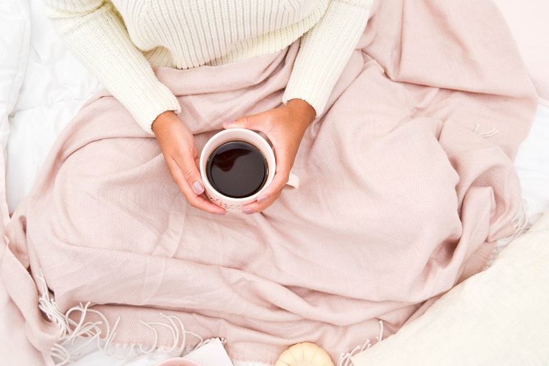 woman holding cup of tea in bed