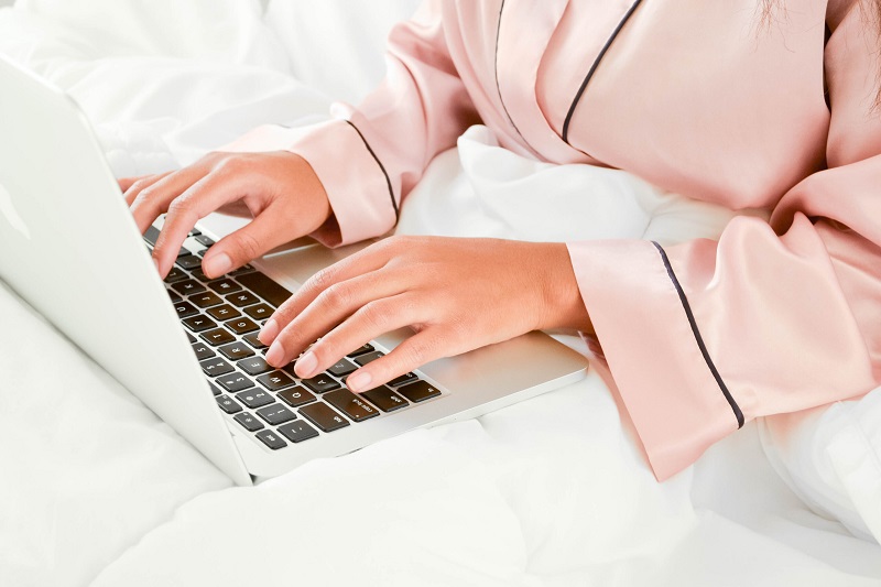 woman in pink pyjamas working on laptop in bed